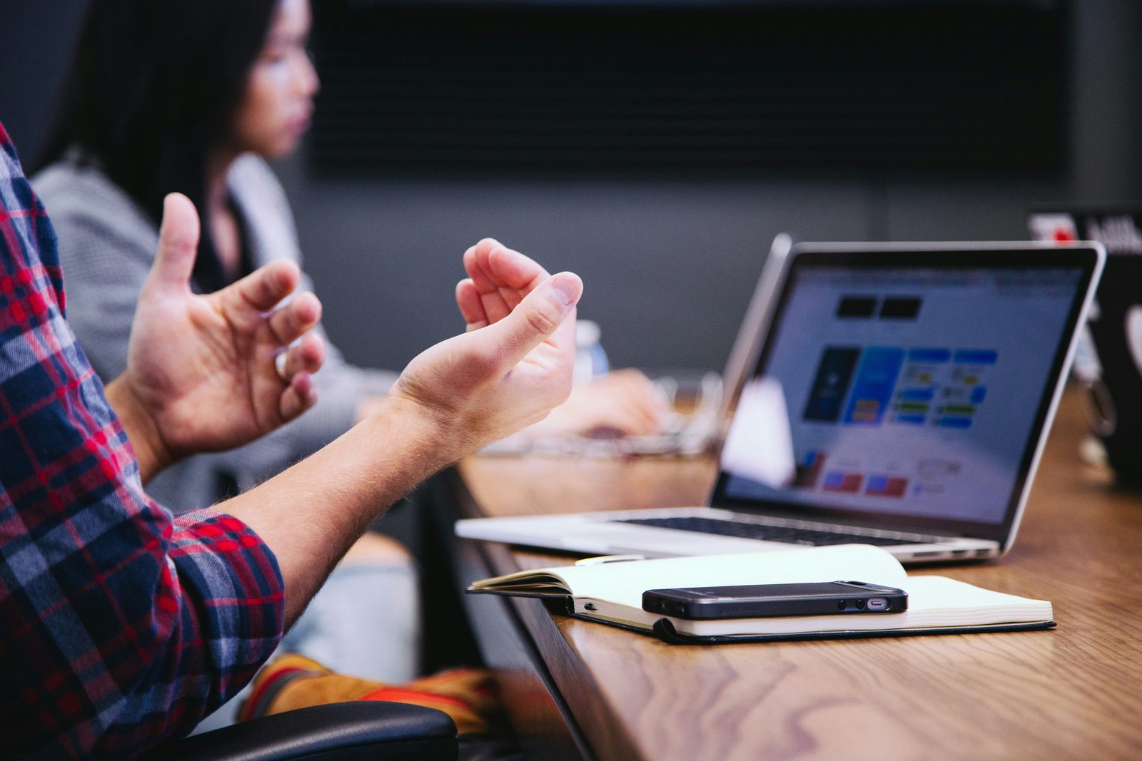 Duas pessoas em conversa à mesa de trabalho, com portátil e caderno